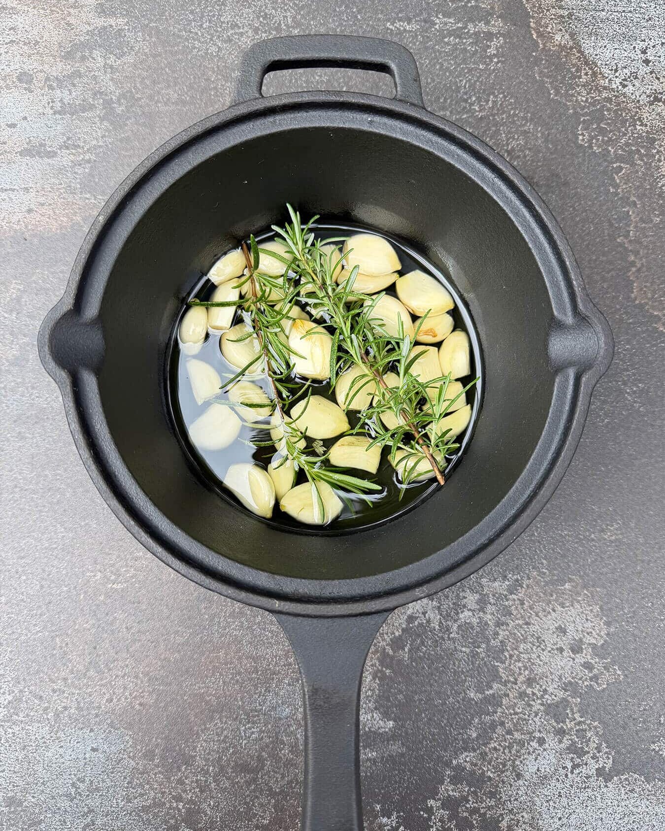 Knoflook en rozemarijn in olie in een gietijzeren pan - Dutch BBQ Dude