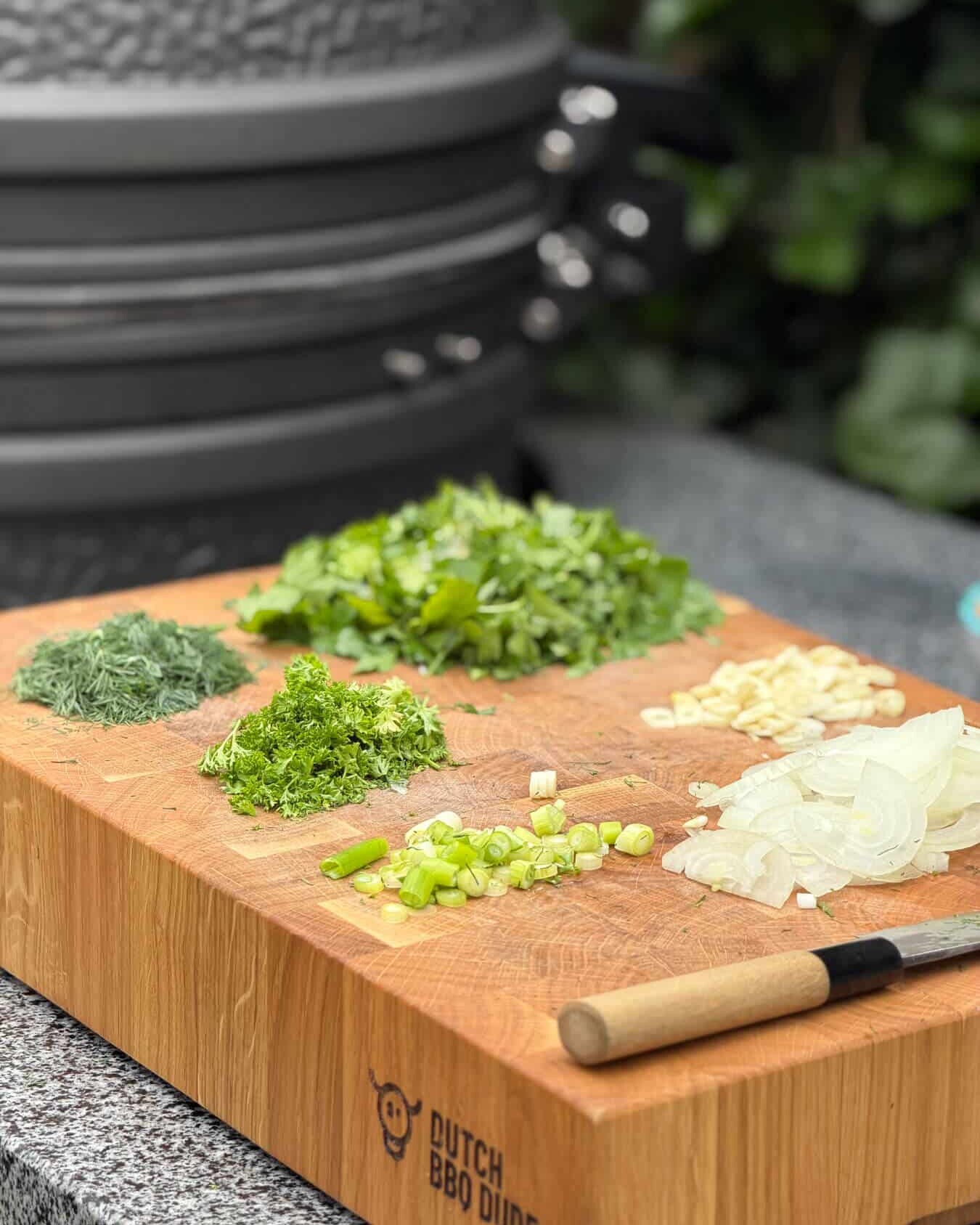 Kruiden en uien op houten snijplank met mes - Dutch BBQ Dude