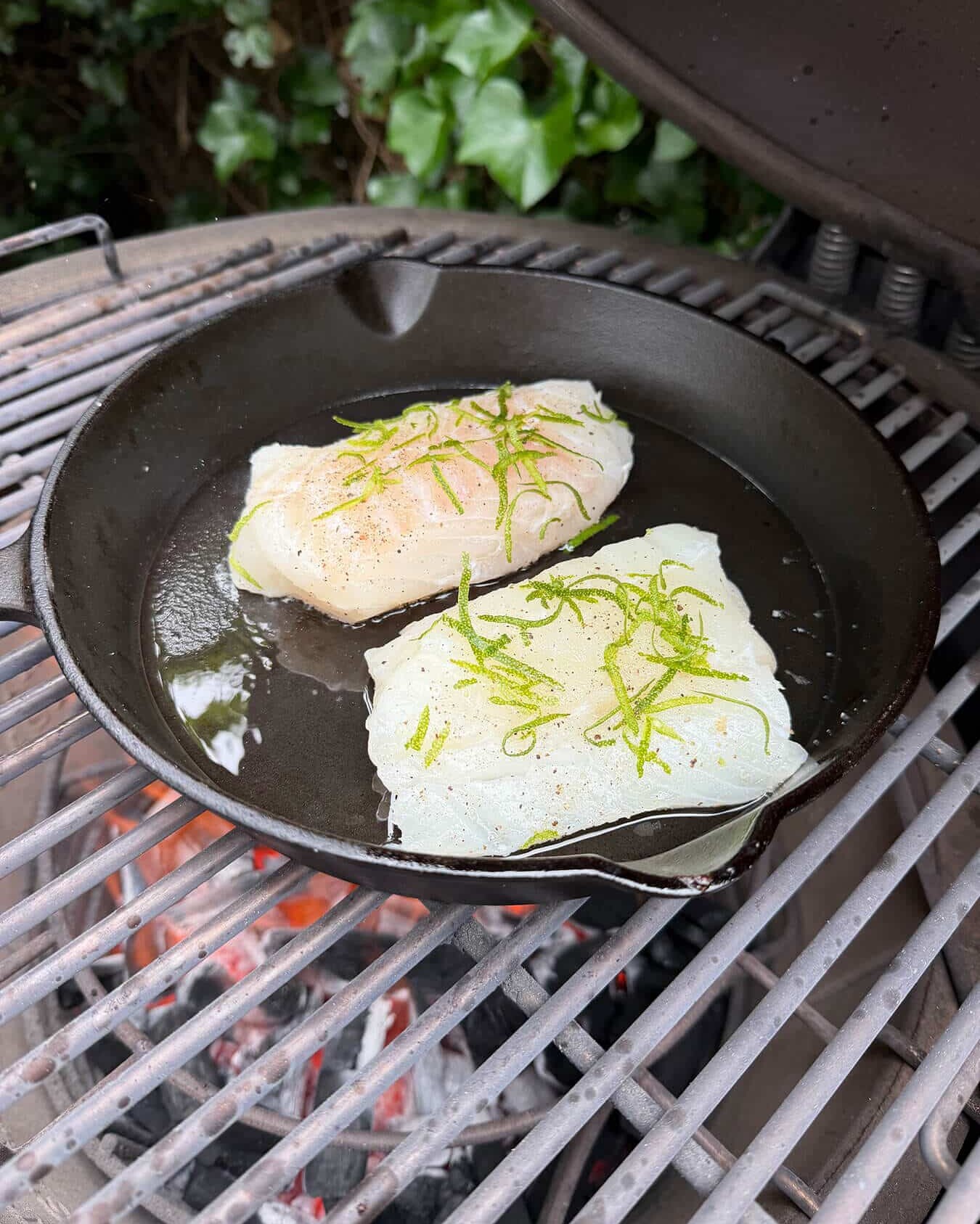 Twee stukken witte vis met limoenrasp in een gietijzeren pan op een grill. - Dutch BBQ Dude